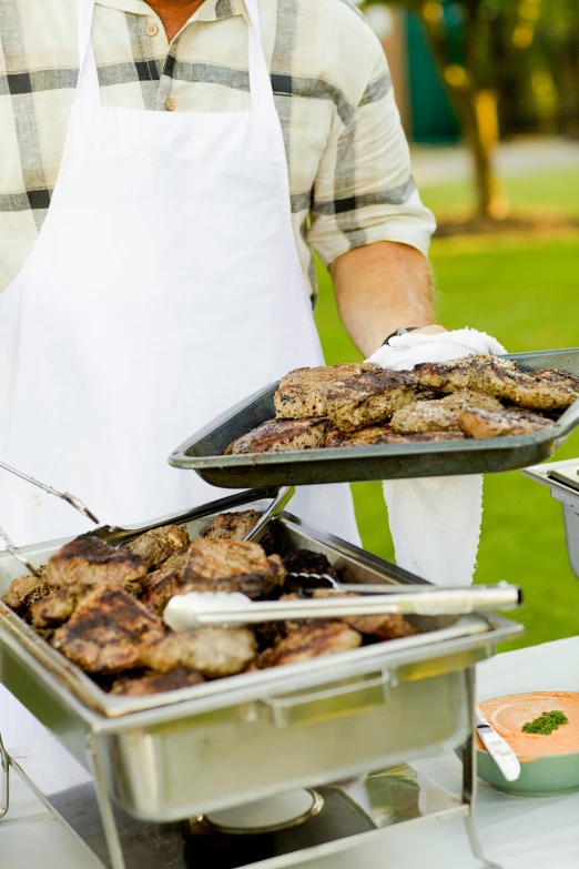 a man in an apron holding two trays of food, grilled chicken, serving burgers, event, square