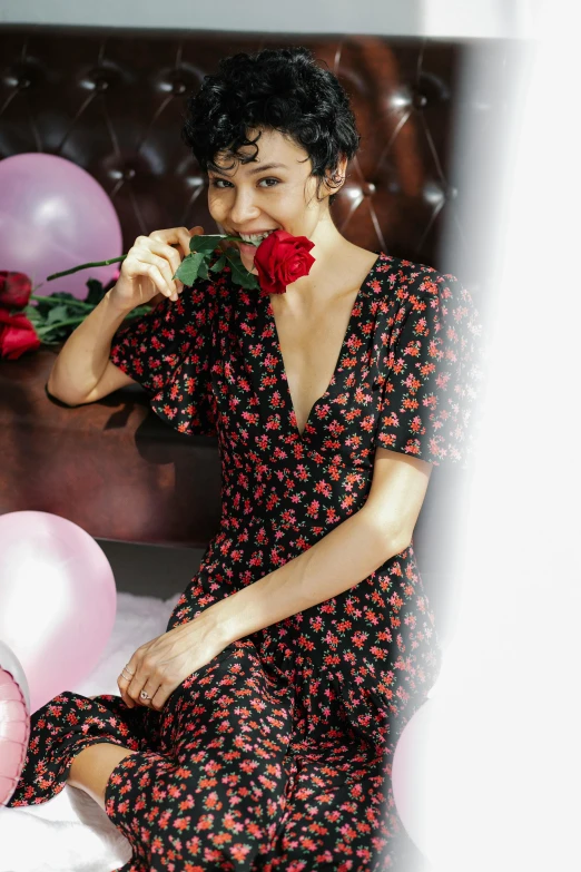 a woman sitting on a bed holding a rose, red floral dress, jumpsuits, zoomed in, black