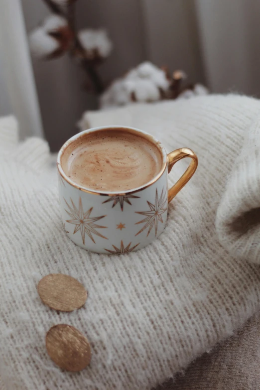 a cup of coffee sitting on top of a blanket, by Julia Pishtar, trending on pexels, art nouveau, festive atmosphere, taupe, galaxy, with a soft