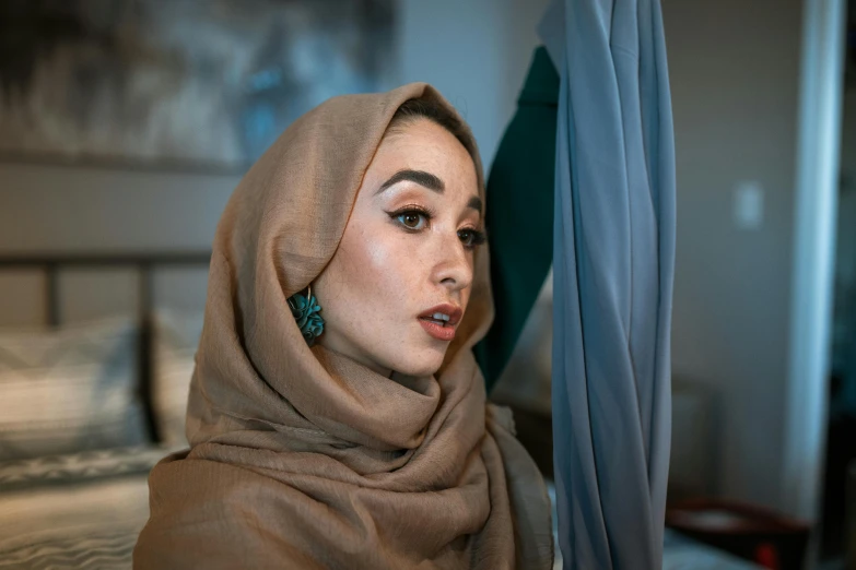 a woman in a hijab sitting on a bed, pexels contest winner, hurufiyya, huge earrings and queer make up, taupe, turqouise, an arab standing watching over