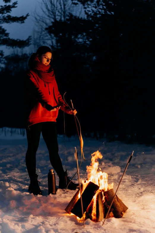 a woman standing next to a fire in the snow, lights on, snacks, holding bow and arrow, lookbook