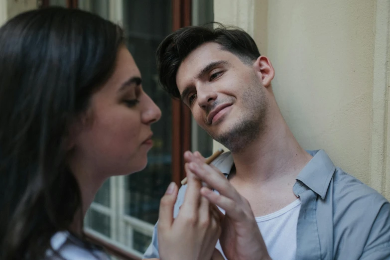 a man smoking a cigarette next to a woman, by Adam Marczyński, pexels contest winner, photorealism, holding his hands up to his face, shy looking down, near a window, non binary model