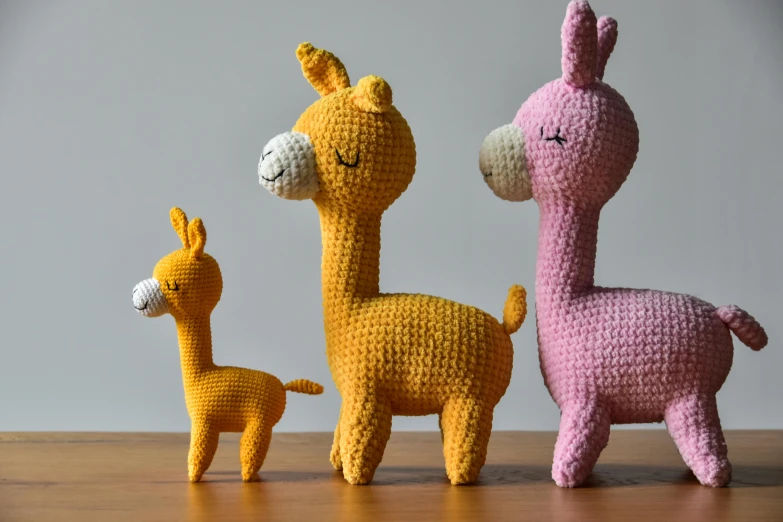 a group of stuffed animals sitting on top of a wooden table, a picture, pink and yellow, alpaca sculpture, 3 colours, crochet