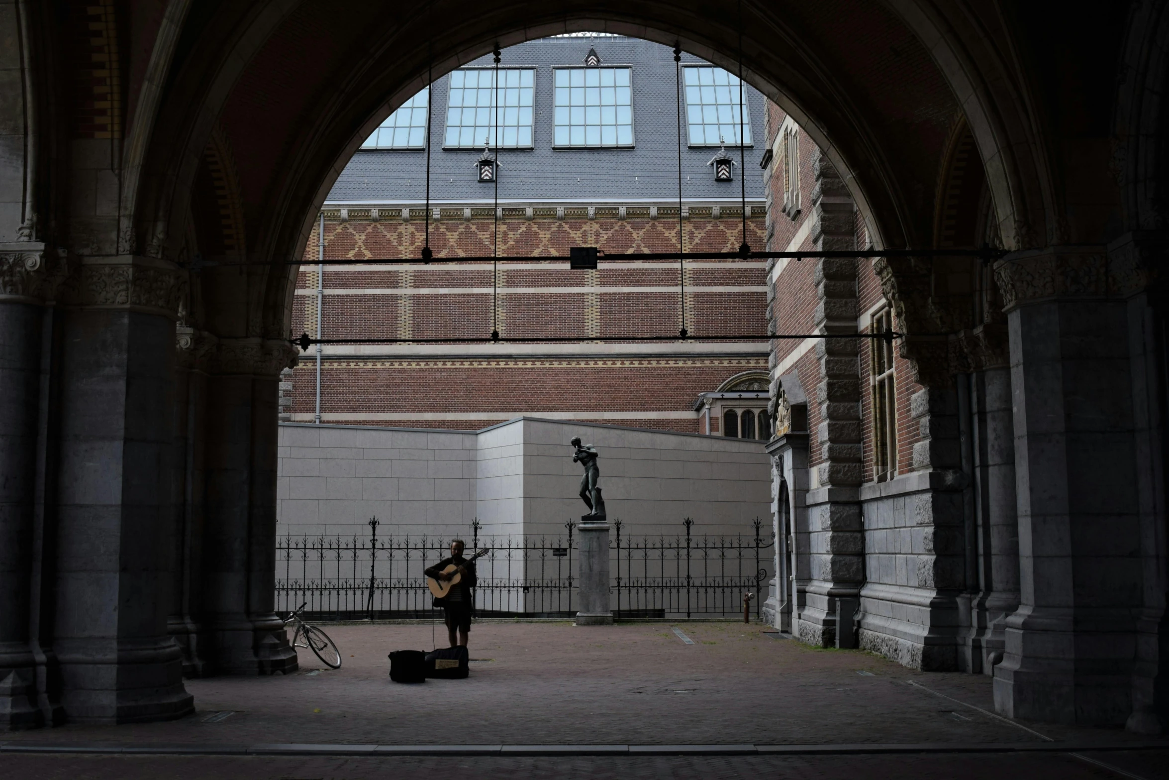 a man that is standing in the middle of a building, a statue, by Jacob Toorenvliet, man playing guitar, dry archways, from the distance, photograph taken in 2 0 2 0