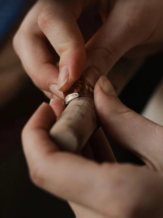 a close up of a person holding a cigar, by Jessie Algie, in a workshop, nordic wedding ring, gold inlay, ignant