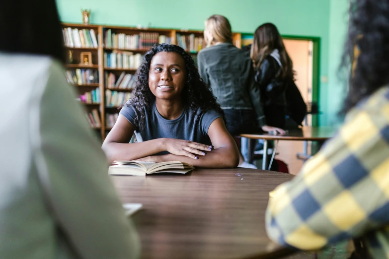 a woman sitting at a table in a library, a portrait, pexels contest winner, happening, black teenage girl, person in foreground, awkward situation, slide show