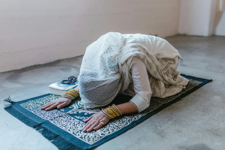 a person laying on a rug on the floor, hurufiyya, praying posture, wearing white silk hood, wearing a sari, stressing out