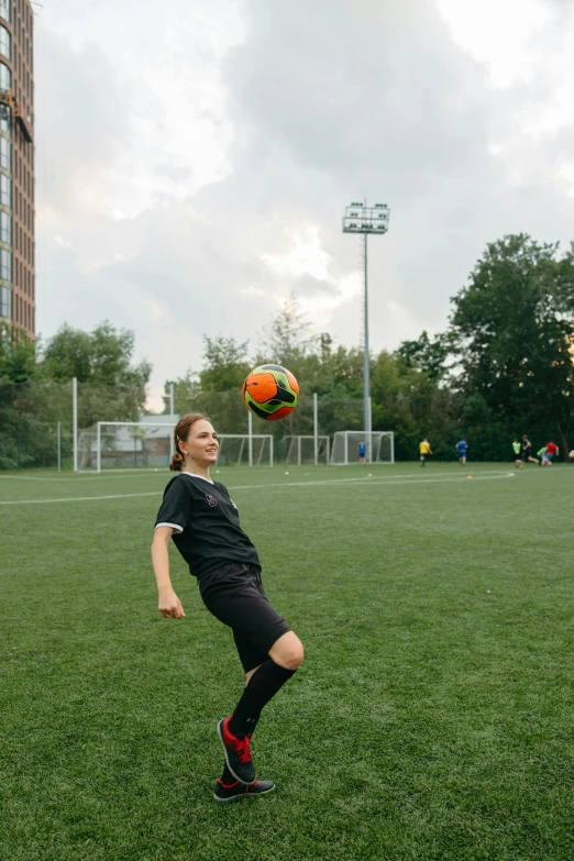 a woman kicking a soccer ball on a field, inspired by Christen Dalsgaard, unsplash, urban surroundings, looking to camera, low quality photo, kreuzberg