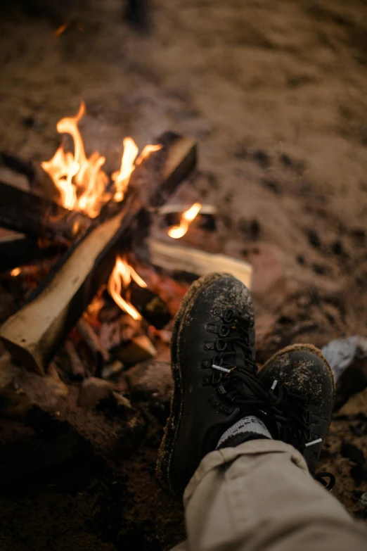 a person's feet in front of a campfire, by Daren Bader, wearing boots, beaching, intensely focused, profile image