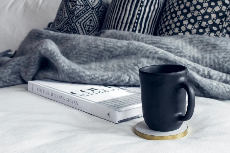 a coffee cup sitting on top of a bed next to a book, a black and white photo, inspired by Louisa Matthíasdóttir, featured on pinterest, round base, matte black, black marble, cosy