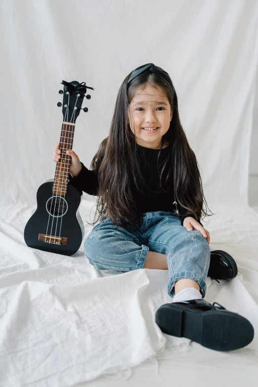 a little girl sitting on a bed holding a guitar, pexels contest winner, wearing a black shirt, japanese collection product, kuntilanak, 2019 trending photo