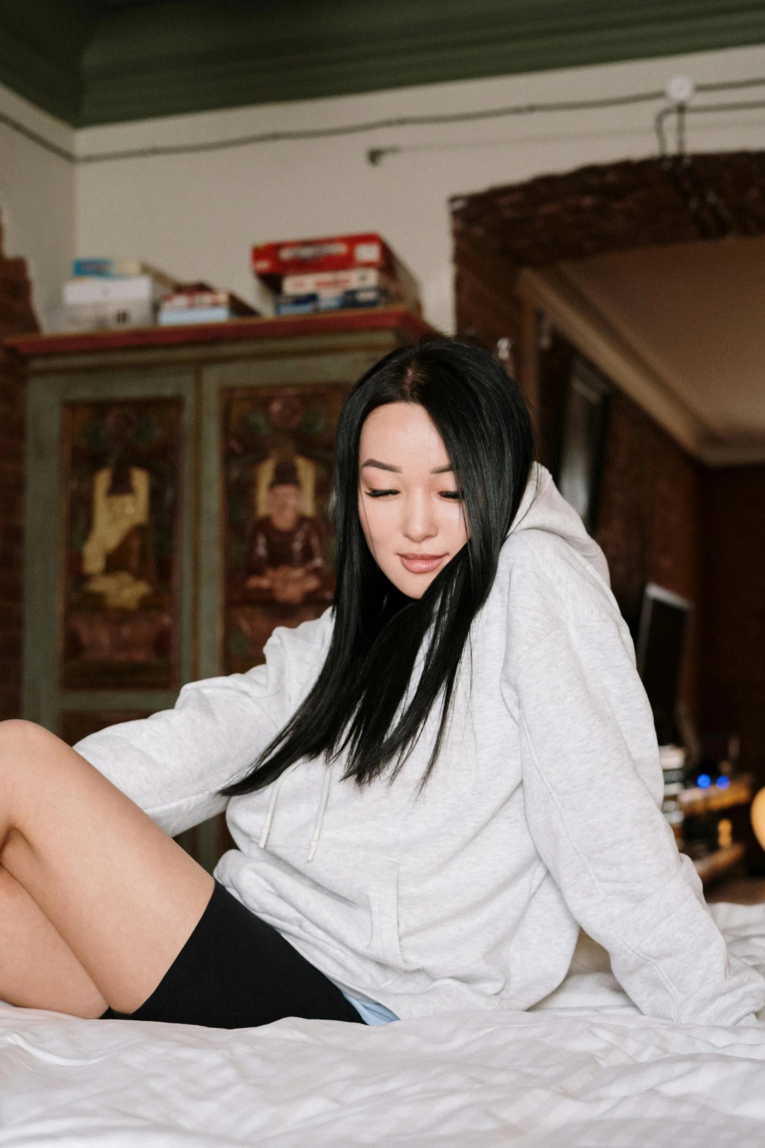 a woman sitting on a bed with her legs crossed, inspired by helen huang, trending on pexels, black haired girl wearing hoodie, white hime cut hairstyle, gif, louise zhang