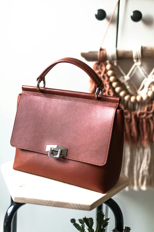 a brown purse sitting on top of a wooden table, inspired by Gaetano Sabatini, featured on instagram, bauhaus, professional product shot, square, feminine, crimson