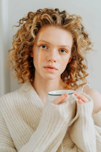 a woman holding a cup in front of her face, by Annabel Eyres, trending on pexels, renaissance, pale skin curly blond hair, wearing turtleneck, photo for a magazine, pensive