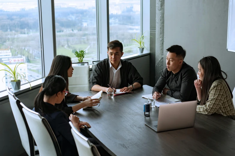 a group of people sitting around a wooden table, sitting on a desk