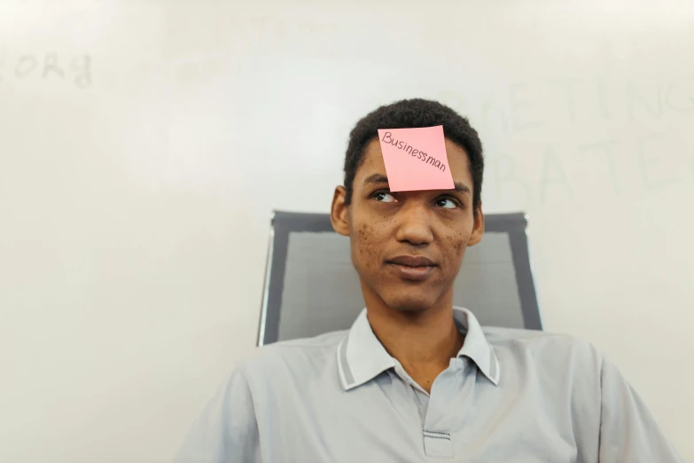 a man with a sticky note on his forehead, an album cover, by Lily Delissa Joseph, unsplash, hyperrealism, sat in an office, mohamed reda, photographed for reuters, a labeled
