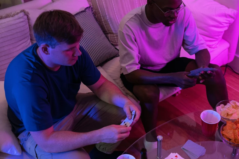 two men sitting on a couch playing a video game, unsplash, process art, playing cards, purple and pink and blue neons, mkbhd, bo burnham