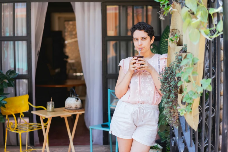 a woman standing outside looking at her cell phone, inspired by Riad Beyrouti, pexels contest winner, renaissance, holding a drink, wearing a camisole and shorts, oona chaplin, standing outside a house