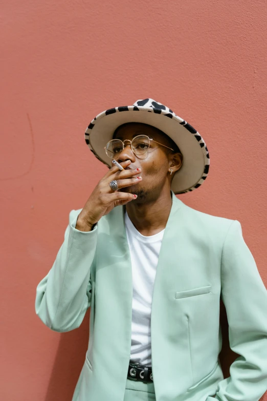 a man in a green suit smoking a cigarette, an album cover, inspired by Barthélemy Menn, trending on pexels, androgynous male, with hat, jamel shabazz, delicate androgynous prince