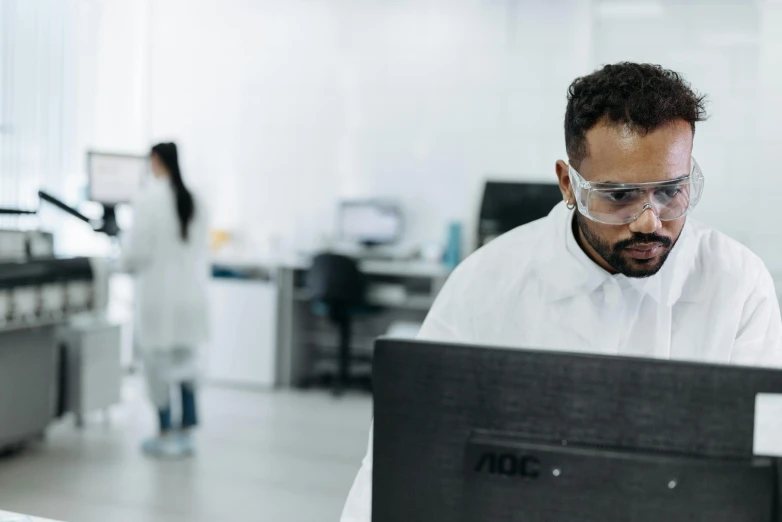 a man in a lab coat working on a computer, pexels, a wide shot, vanta blac, profile image, brown