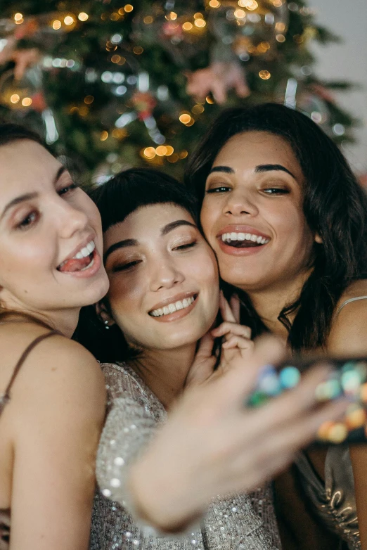 three women taking a selfie in front of a christmas tree, by Julia Pishtar, trending on pexels, with sparkling gems on top, brunettes, a still of a happy, gen z