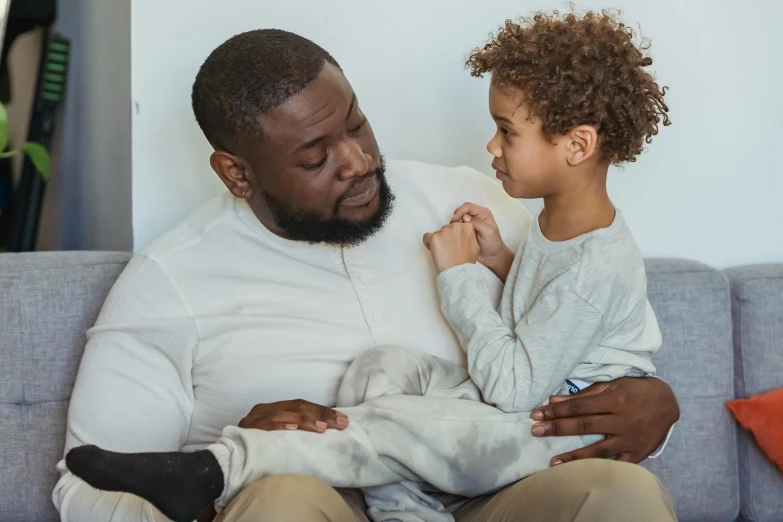 a man sitting on a couch holding a small child, pexels contest winner, incoherents, african american, looking her shoulder, sitting on the edge of a bed, game ready