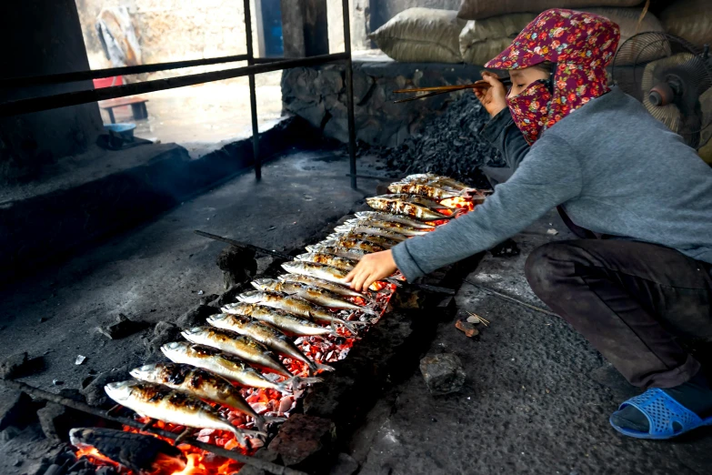 a woman cooking fish on an open fire, by Julia Pishtar, pexels contest winner, hurufiyya, balaclava, having a snack, avatar image, smelters