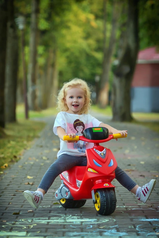 a little girl riding on the back of a red scooter, pexels contest winner, ukrainian girl, 15081959 21121991 01012000 4k, in a park, sitting on a motorcycle