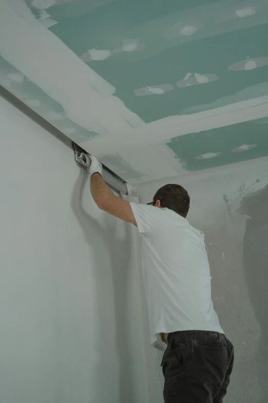 a man that is standing on a ladder, painting on the ceiling, walls are made of dry wall, promo image, low quality photo