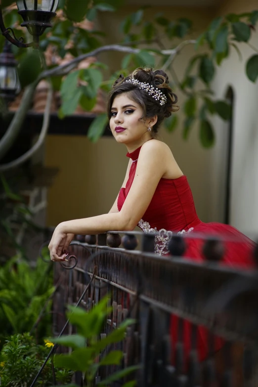 a woman in a red dress leaning on a fence, a portrait, by reyna rochin, pexels contest winner, wearing a tiara, tlaquepaque, indoor picture, 1 6 years old