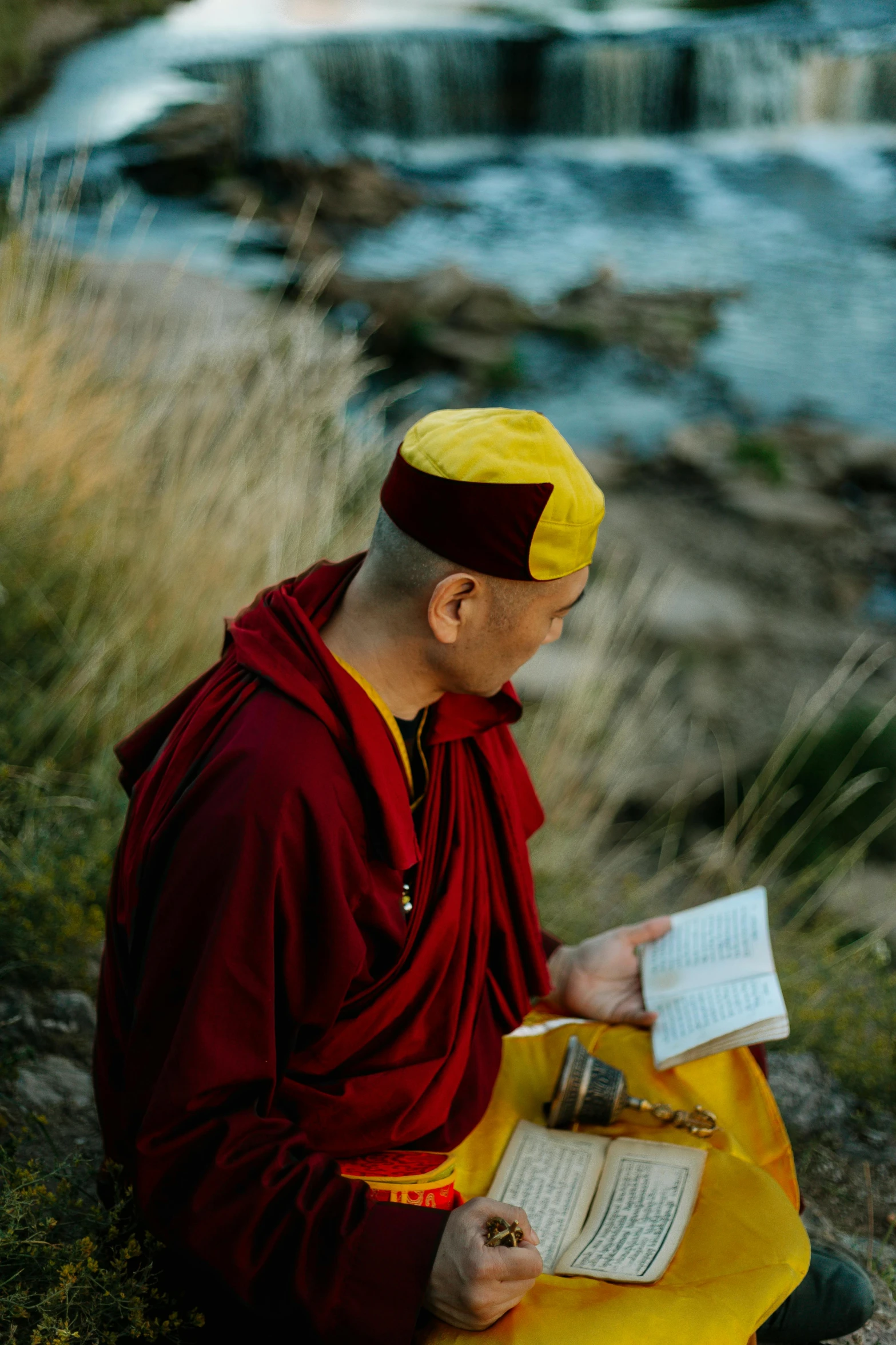 a man sitting on a rock reading a book, wearing red and yellow clothes, monk clothes, portrait featured on unsplash, high-quality photo
