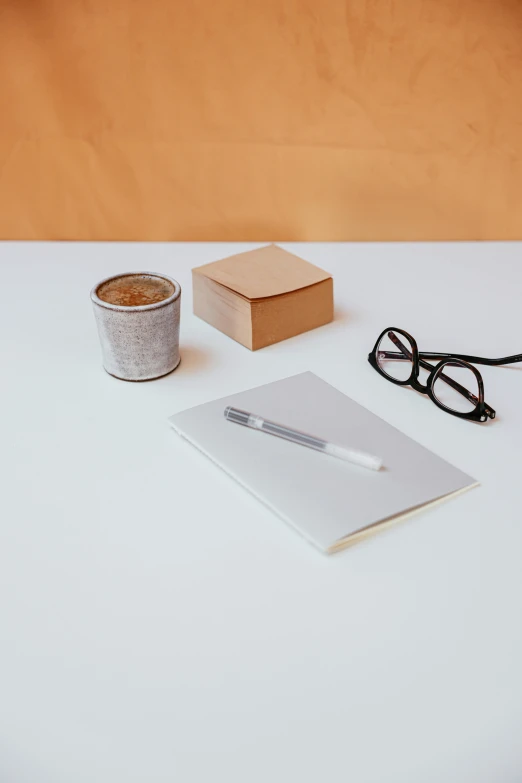 a cup of coffee and a notebook on a table, a minimalist painting, by Harvey Quaytman, trending on unsplash, cigarrette boxes at the table, design on white background, background image, no - text no - logo