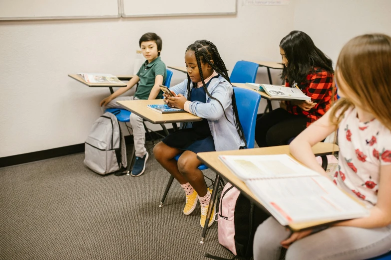 a group of children sitting at desks in a classroom, by Carey Morris, pexels contest winner, checking her phone, siting in a chair, diverse, carson ellis