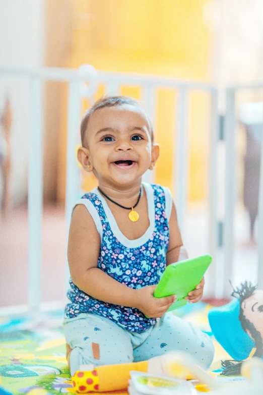 a baby sitting on the floor playing with a toy, an album cover, pexels contest winner, indian girl with brown skin, looking at his phone, happily smiling at the camera, activity play centre