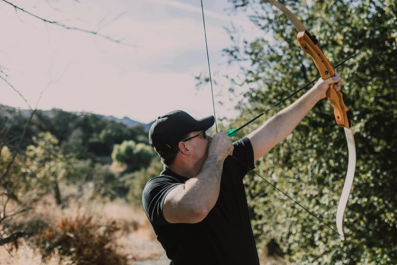 a man in black shirt holding a bow and arrow, unsplash, malibu canyon, launching a straight ball, food. craft and adventure, profile pic