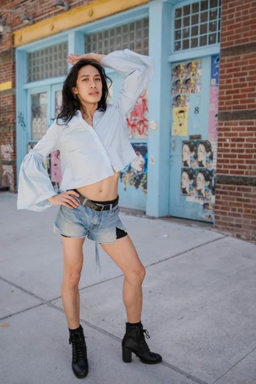 a woman posing for a picture in front of a building, croptop and shorts, wearing a light blue shirt, queer woman, julia sarda