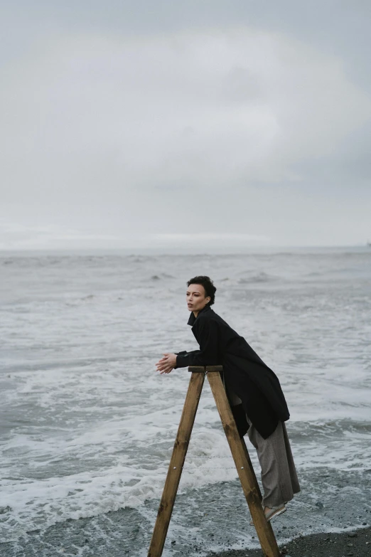 a woman standing on a ladder in front of the ocean, inspired by Peter Lindbergh, romanticism, norilsk, a cold, sittin, beautiful caitriona balfe