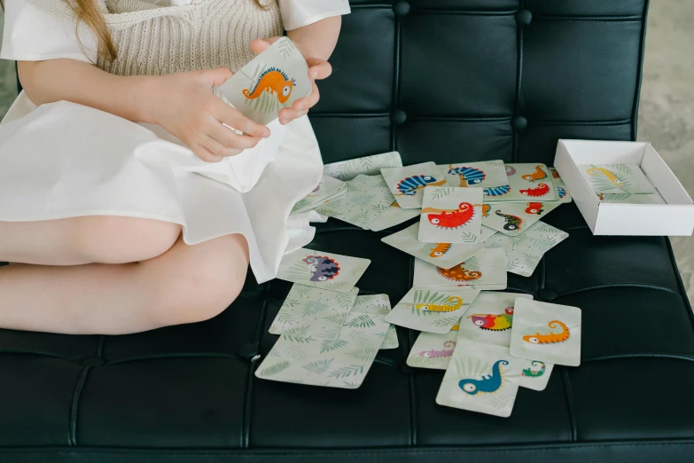 a woman sitting on a chair next to a pile of playing cards, a jigsaw puzzle, by Emma Andijewska, dinosaurs, toddler, medium close up, tabletop game board