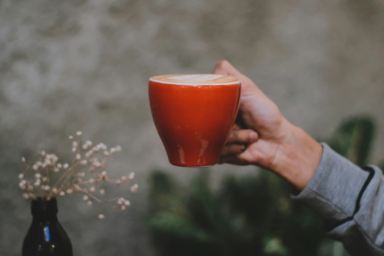 a person holding a cup of coffee in their hand, by Emma Andijewska, pexels contest winner, payne's grey and venetian red, al fresco, vibrant orange, background image