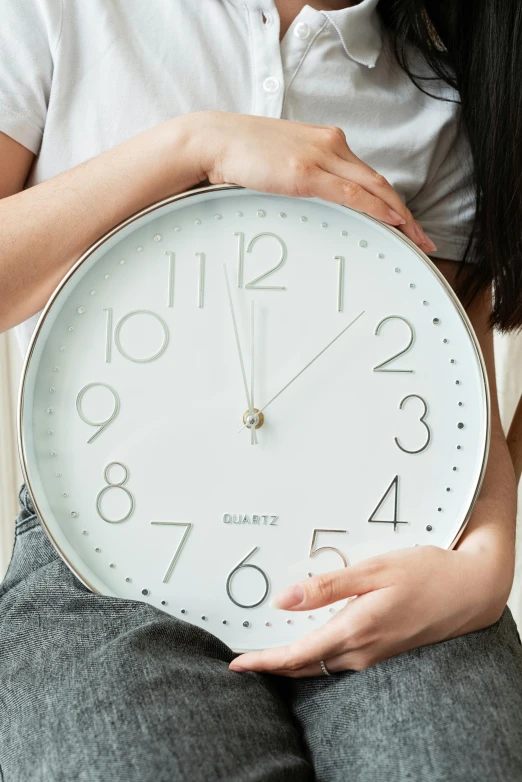 a woman sitting on a couch holding a clock, by Julia Pishtar, trending on pexels, minimalism, silver，ivory, extra wide, pastel', countdown