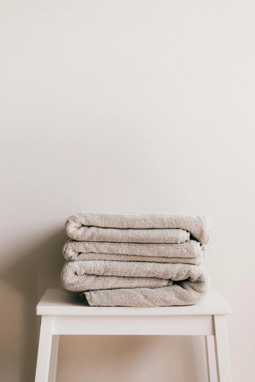 a stack of towels sitting on top of a white stool, trending on pexels, minimalism, taupe, robes, melting, portrait shot