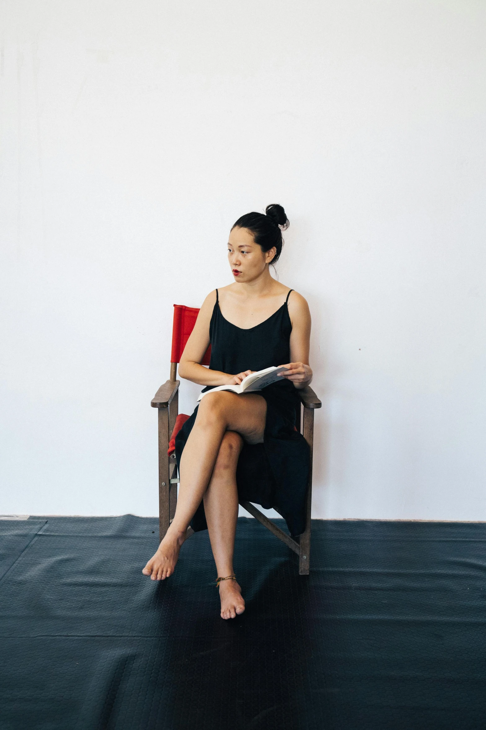 a woman sitting in a chair reading a book, a portrait, inspired by Fei Danxu, unsplash, process art, she is wearing a black tank top, in a photo studio, legs crossed, phuoc quan