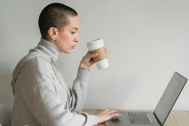 a woman sitting at a table with a laptop and a cup of coffee, brown buzzcut, profile image, grey, cardboard