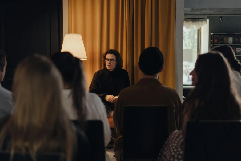 a group of people sitting in chairs in a room, an album cover, by Jacob Toorenvliet, unsplash, giving a speech, joe keery, ignant, standing in class