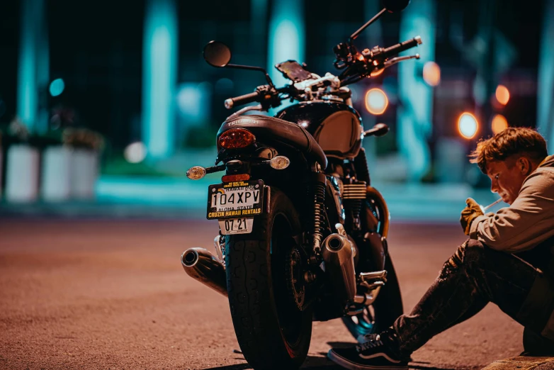 a man sitting on the ground next to a motorcycle, by Tom Bonson, pexels contest winner, tail lights, triumph, manly, night time footage