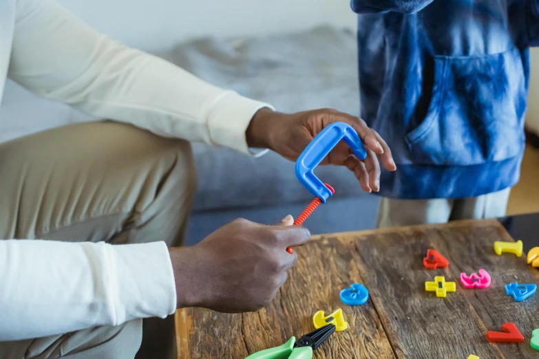 a man playing with plastic letters on a table, by Julian Allen, pexels contest winner, holding a crowbar, children playing with pogs, 3d printed, looking across the shoulder