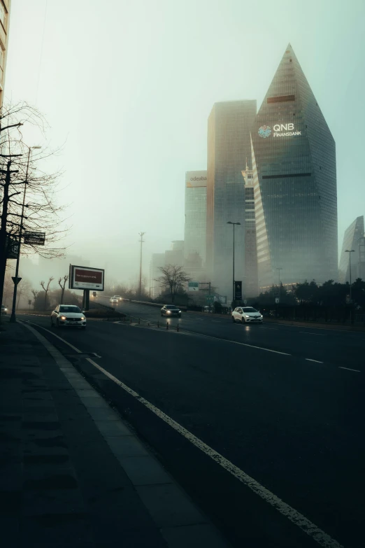 a group of cars driving down a street next to tall buildings, a matte painting, pexels contest winner, hazy morning foggy, mongolia, ((mist)), 4 k cinematic photo