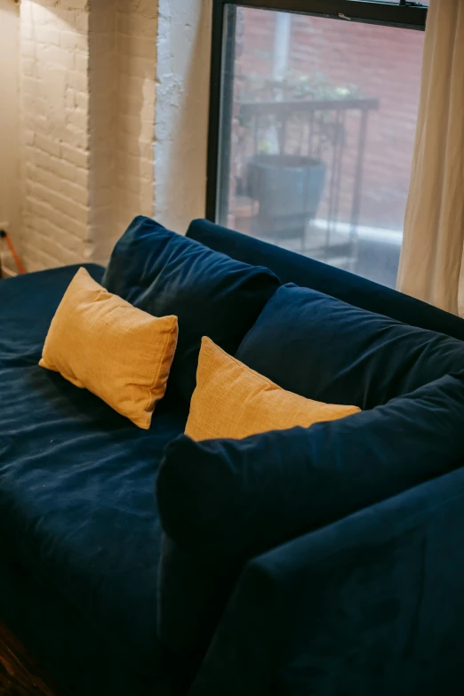 a blue couch sitting in a living room next to a window, by Adam Marczyński, some sandy yellow pillows, low quality photo, multiple stories, apartment