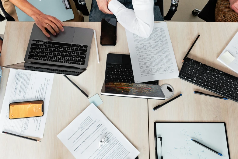 a group of people sitting around a table with laptops, by Carey Morris, trending on pexels, piles of paperwork, minimalist desk, background image, maintenance photo