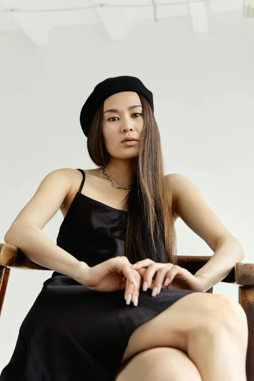 a woman in a black dress sitting in a chair, inspired by Wang E, trending on pexels, black beanie, half asian, wearing a camisole, long flat hair